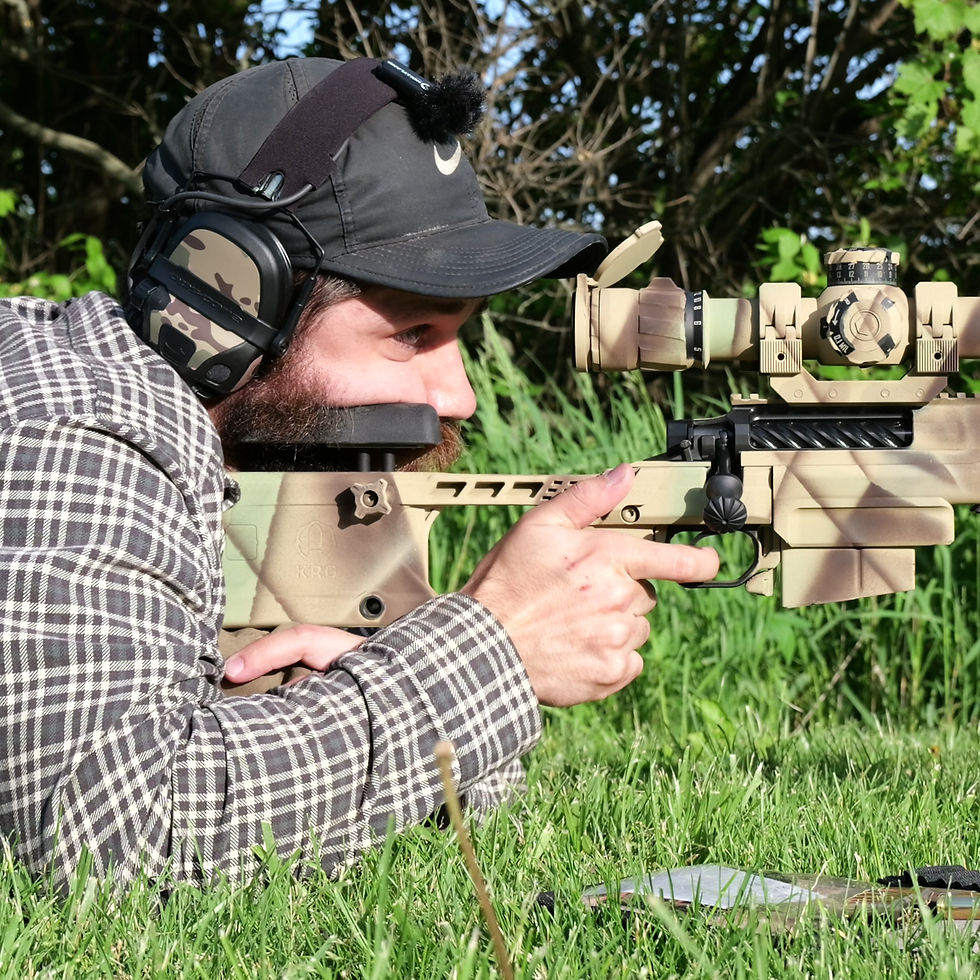 A man wearing a flannel shirt and a black hat takes aim with a precision rifle from the prone position