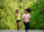 Two women smiling and jogging together on a park trail.