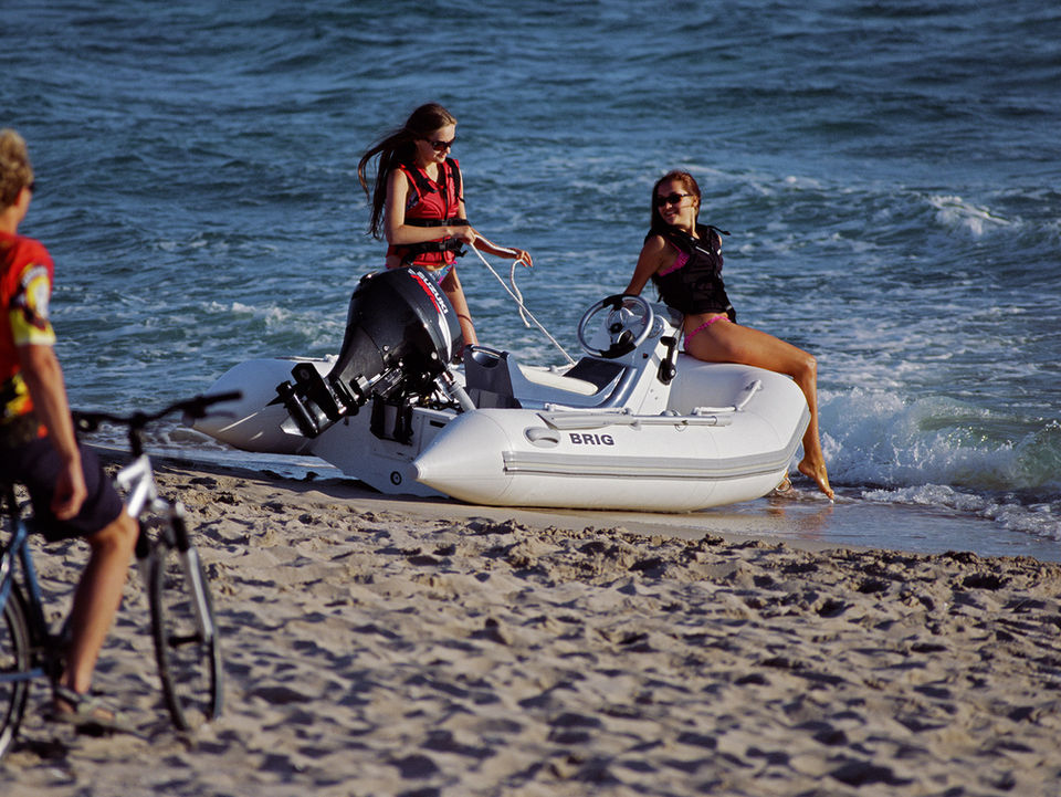 Man on bike watches two women with Falcon 330 boat on beach