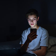 Teen boy looking at smartphone in his hand in dark bedroom.jpg