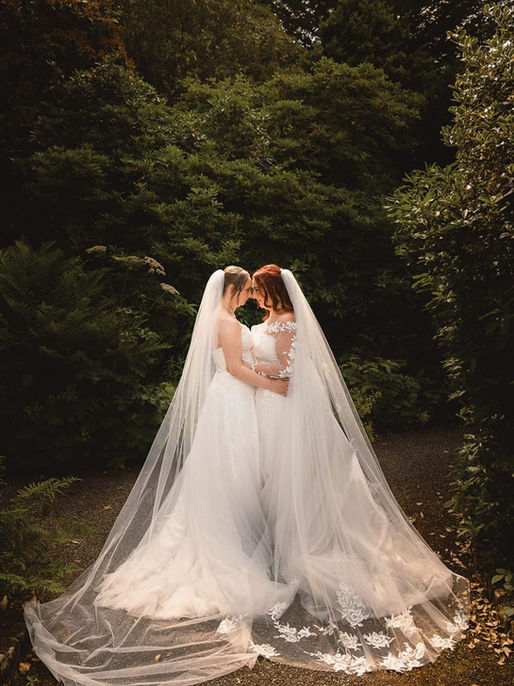 Two brides in wedding dresses holding hands and laughing, captured during their wedding day celebration.