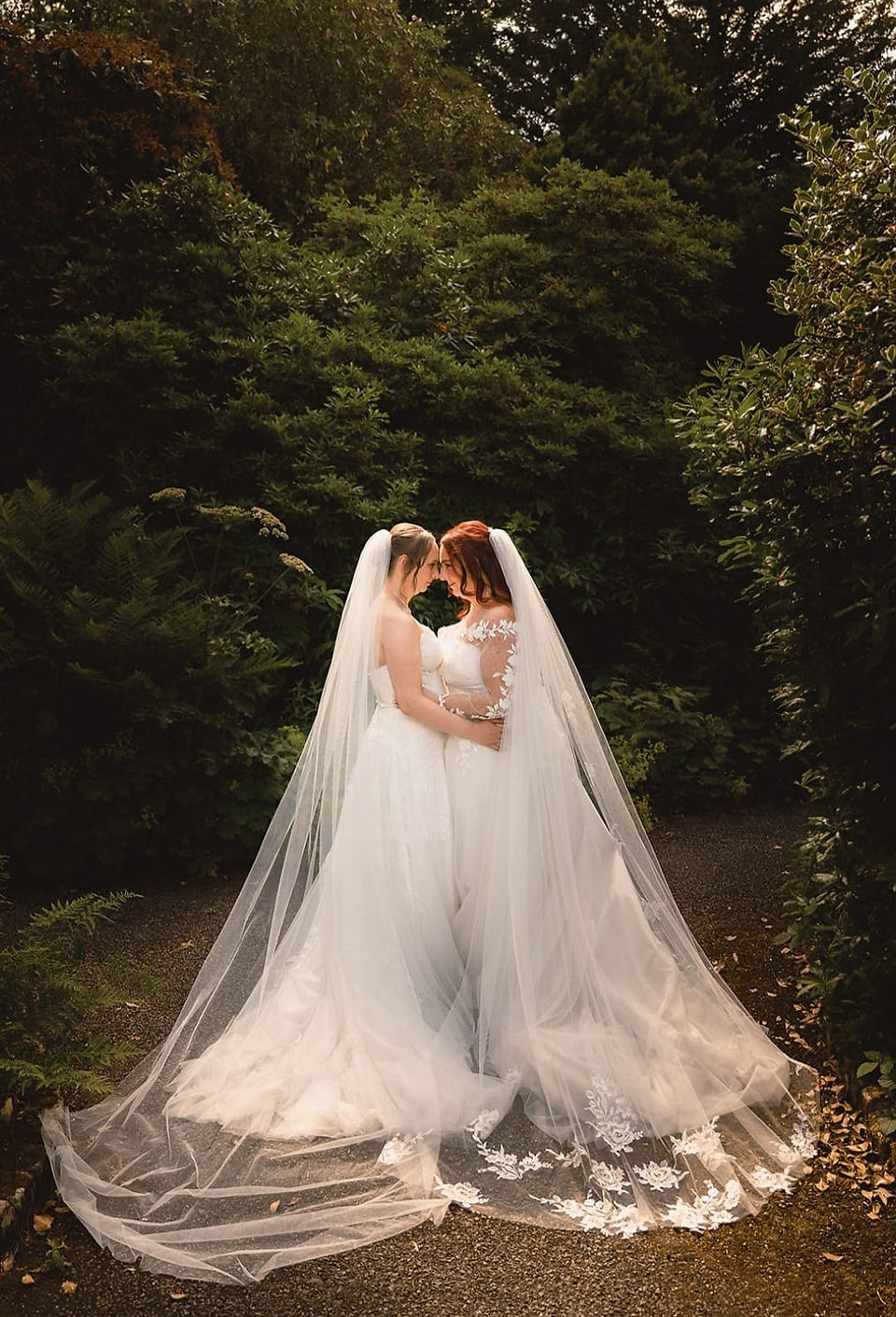 Two brides smiling together in their wedding gowns, celebrating their wedding day surrounded by love.