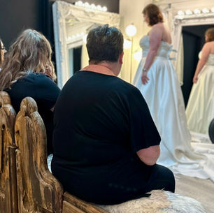 Plus size bride laughing with her stylist while trying on a romantic embroidered wedding dress in the boutique.