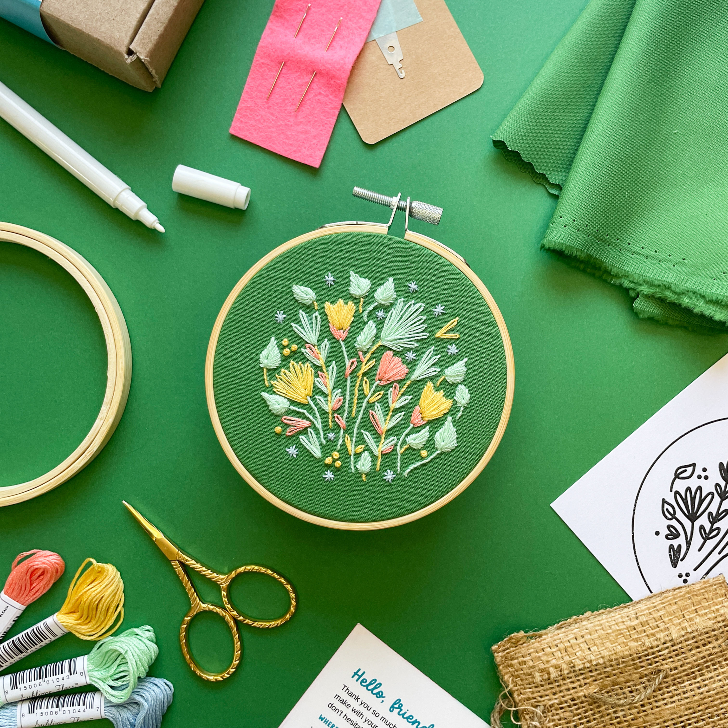 Embroidery kit for a project featuring pastel flowers in blues, greens, pinks, and yellows, on a dark green cotton fabric.