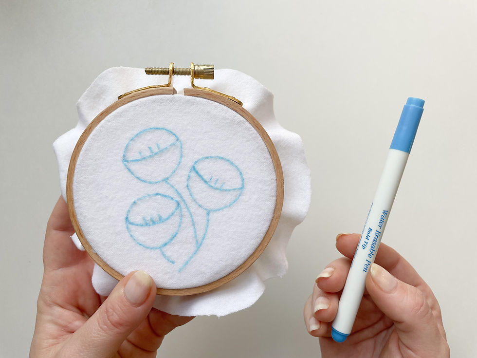 Hope holds up an embroidery hoop with three tulips drawn onto a white flannel fabric with a blue pen.