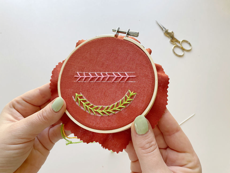 Hope is holding up a hoop with pink, green, and yellow vines stitched on orange fabric.