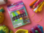 Box of "friendship bracelet floss" in a rainbow of colors, on a pink surface and surrounded by embroidery supplies.