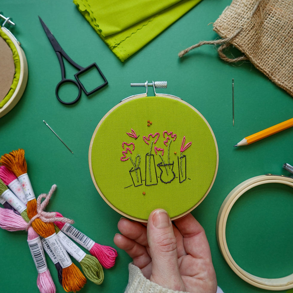 Embroidery project featuring four simple pink flower buds in vases stitched onto bright green fabric.