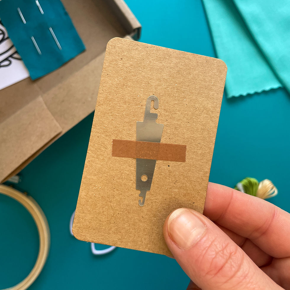 Thumbnail: Embroidery kit for a project featuring a satin stitched potted cactus in green with brown spikes, on bright blue fabric.