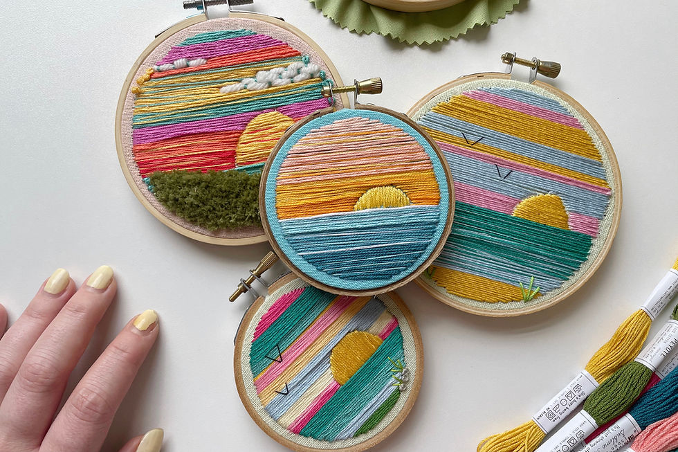 A photo of four embroidery hoops featuring landscapes stitched with vibrant colors.