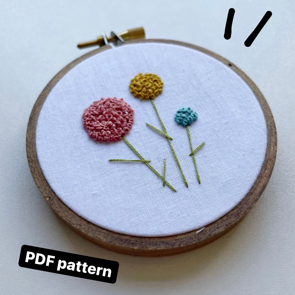 A photo of three embroidered flowers in pink, yellow, and blue, with green stems.