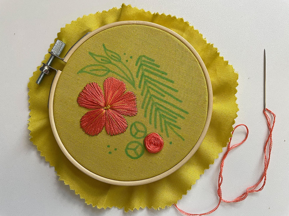 Hope's initial flower is now fully stitched in that orange-peach color with yellow highlights and center; now, she's added a single rose in the same color.
