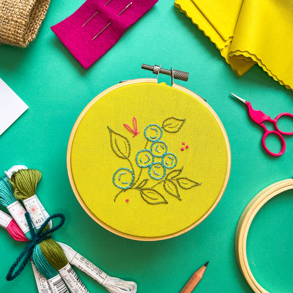 Embroidery project with simple blueberry bush stitched onto yellow green cotton fabric and surrounded by kit supplies.