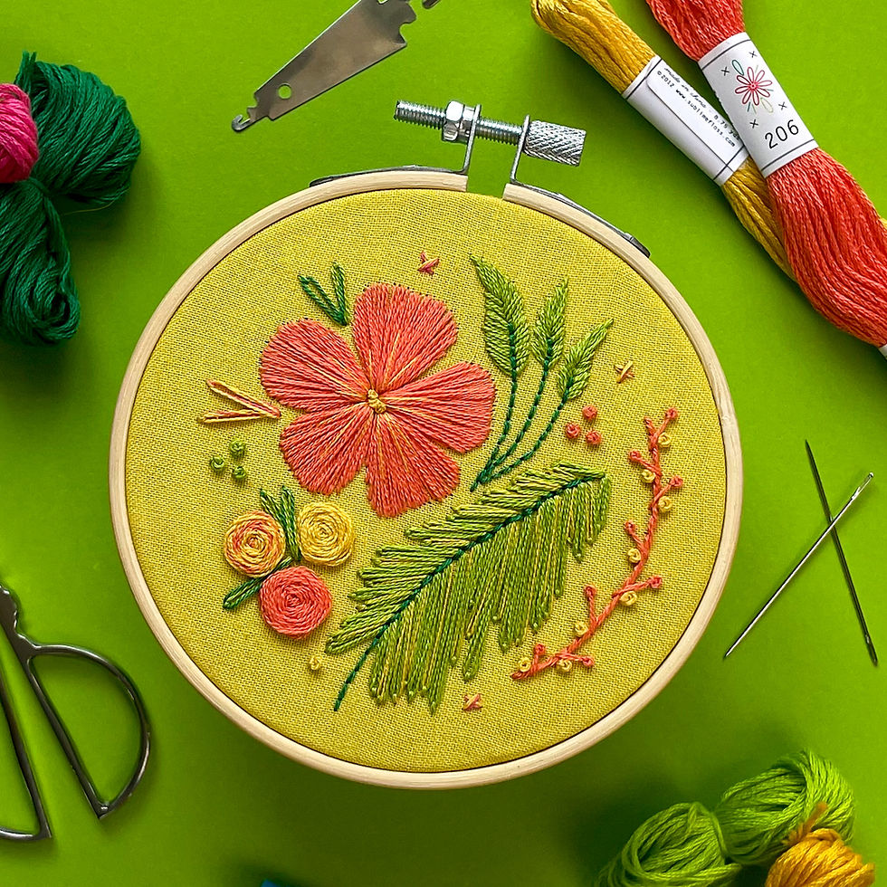 An embroidery project with flowers, vines, and leaves in bright oranges, yellows, pinks, and greens, stitched onto a bright green fabric.