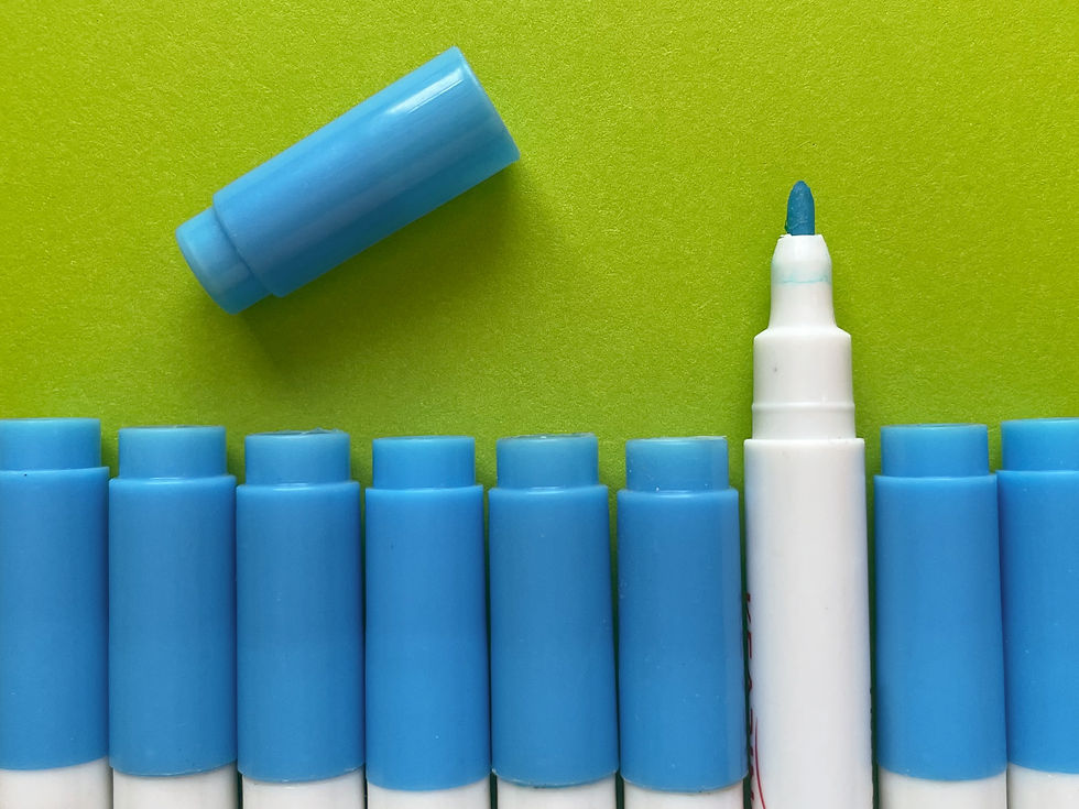 Blue water-erasable transfer pens on a green background; one has its cap off, revealing a bright blue tip.