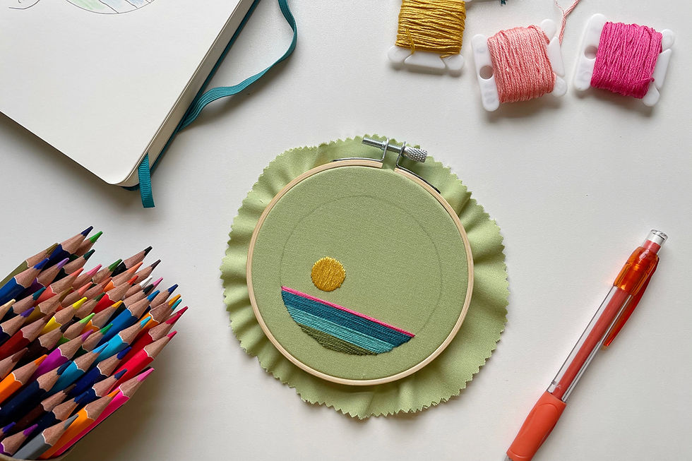 A photo of an unfinished embroidery project surrounded by color pencils, embroidery floss, and a notebook.
