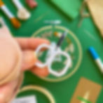 Thumbnail: Embroidery kit and finished project with a design featuring a snowy tree and wintery wreath on green cotton fabric.