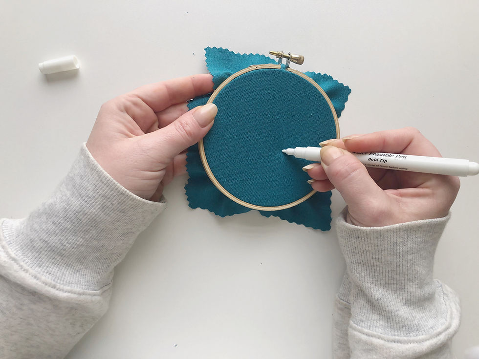 Hope uses a white pen to draw a curved line onto her dark blue linen fabric.