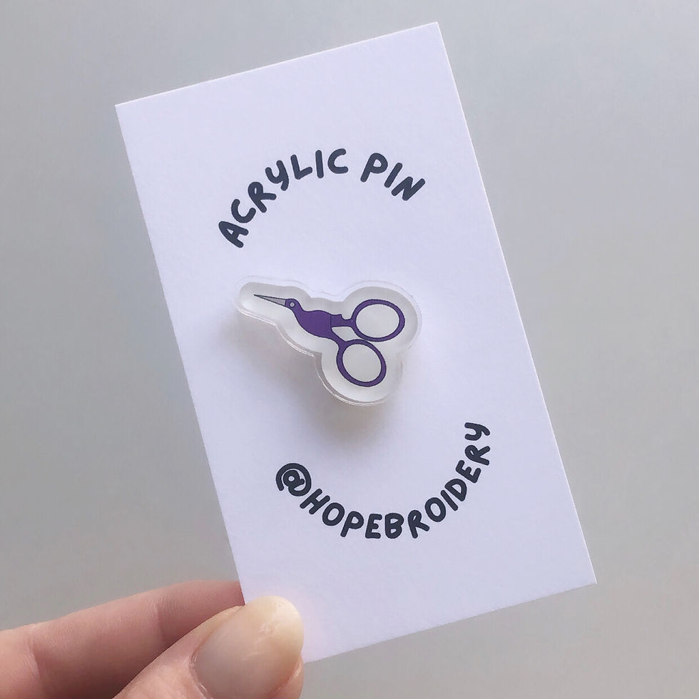 Purple stork scissors acrylic pin on a backing card that reads, "acrylic pin," and "@hopebroidery"