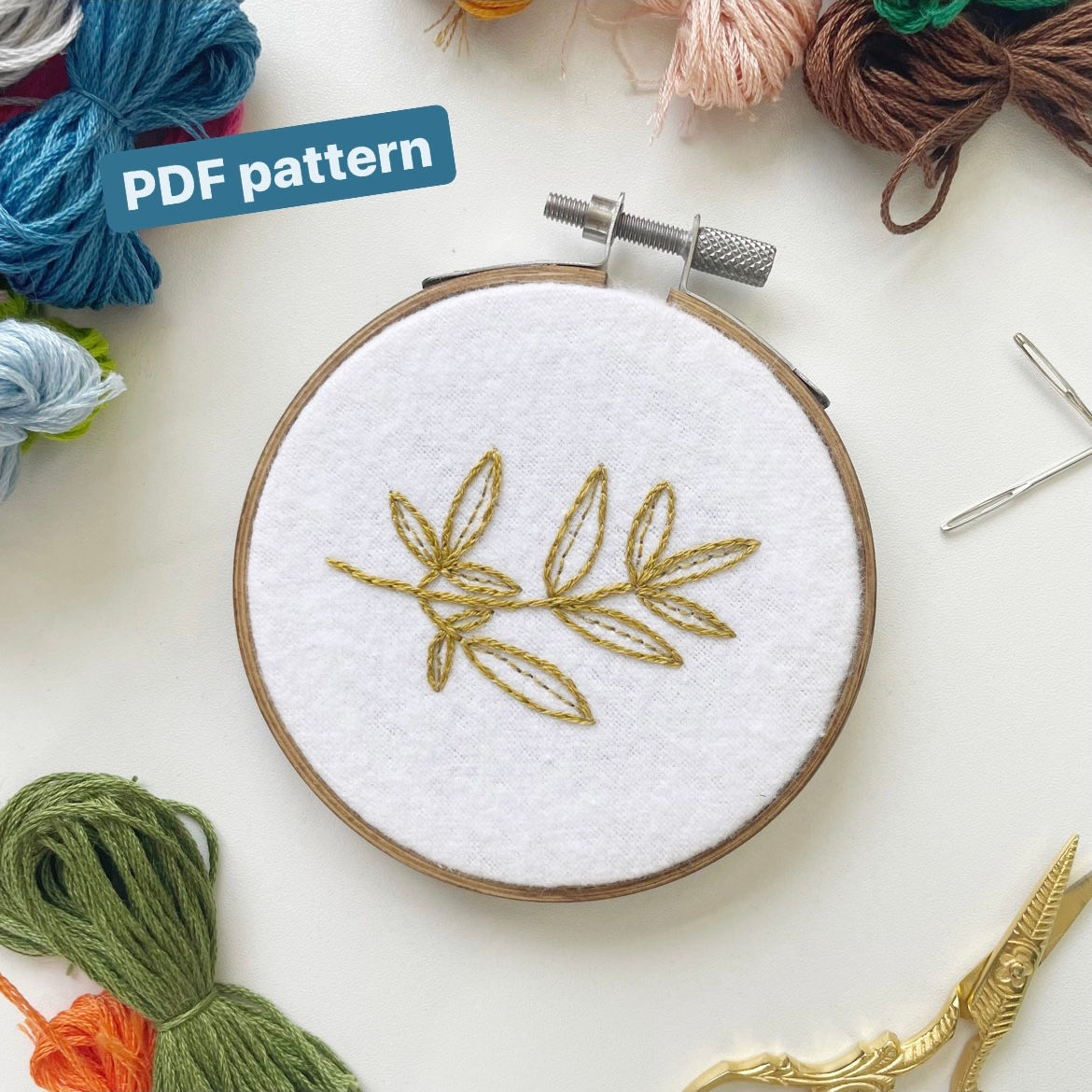 Embroidery hoop with a light olive green leafy vine stitched onto white flannel fabric.