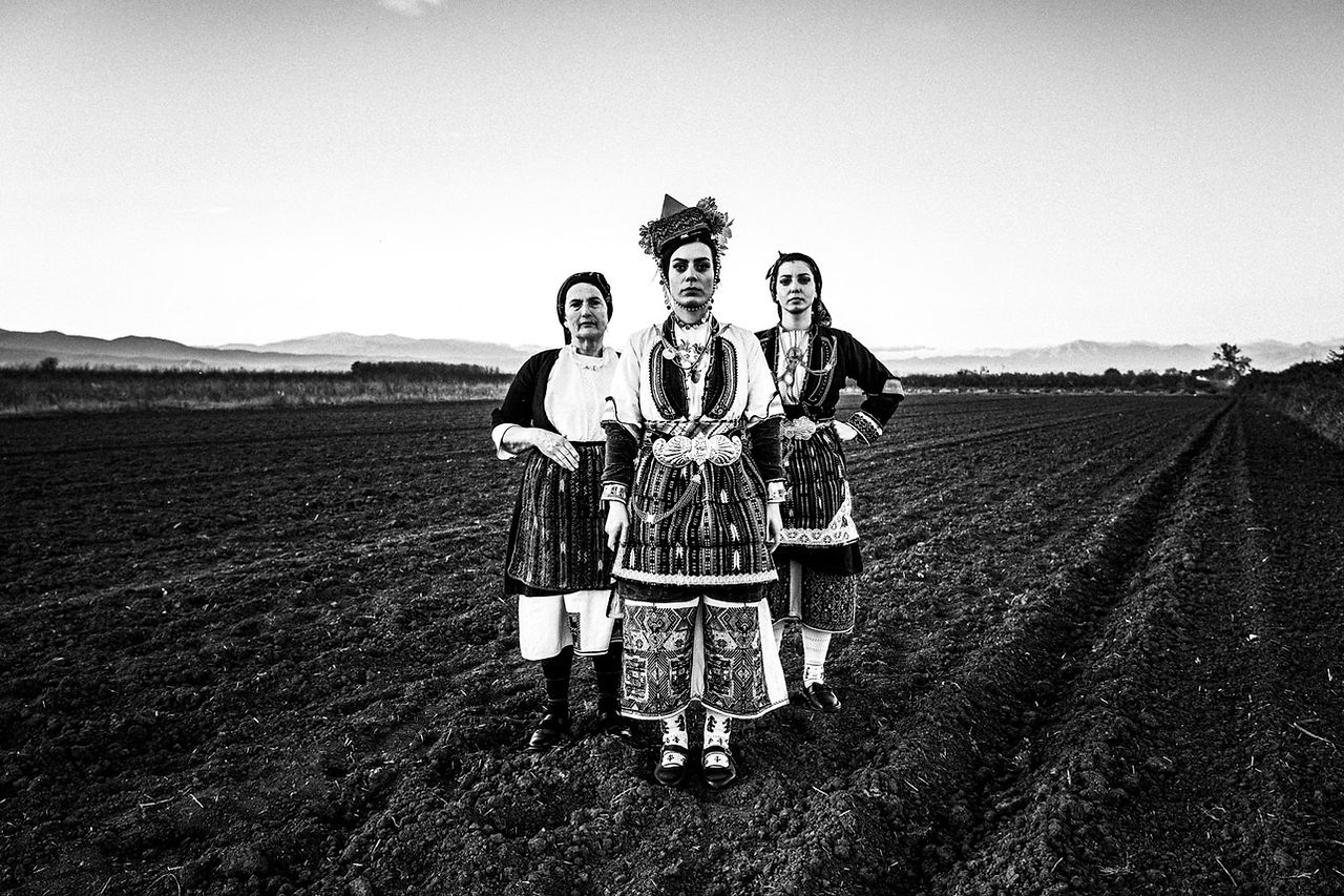 Three women at a local field, wearing the traditional costumes. Aggelochori, Naoussa, Macedonia, Greece. Black and white photograph by George Tatakis
