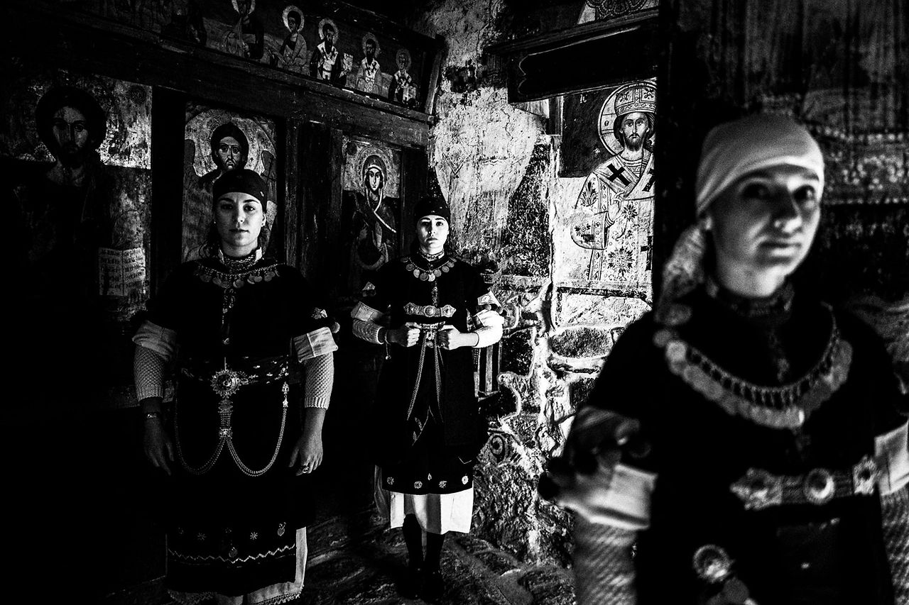 Three women in a dark local church at Prespes, Macedonia, Greece. Black and white photograph by George Tatakis