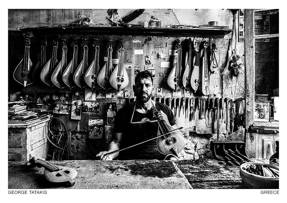 A man posing in his workshop in Rethymnon, on the island of Crete, Greece. He manufactures and mends traditional lyra instruments. Black and white photography postcard by George Tatakis, project Ethos.