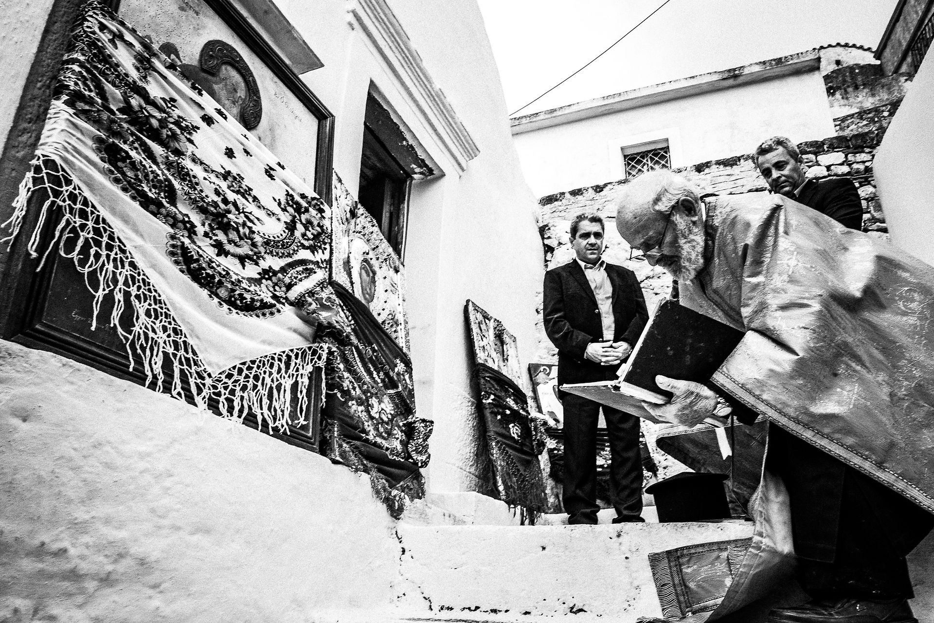 The local priest kneeling before a local church on Easter Tuesday. Olympos, Karpathos, Greece. 
