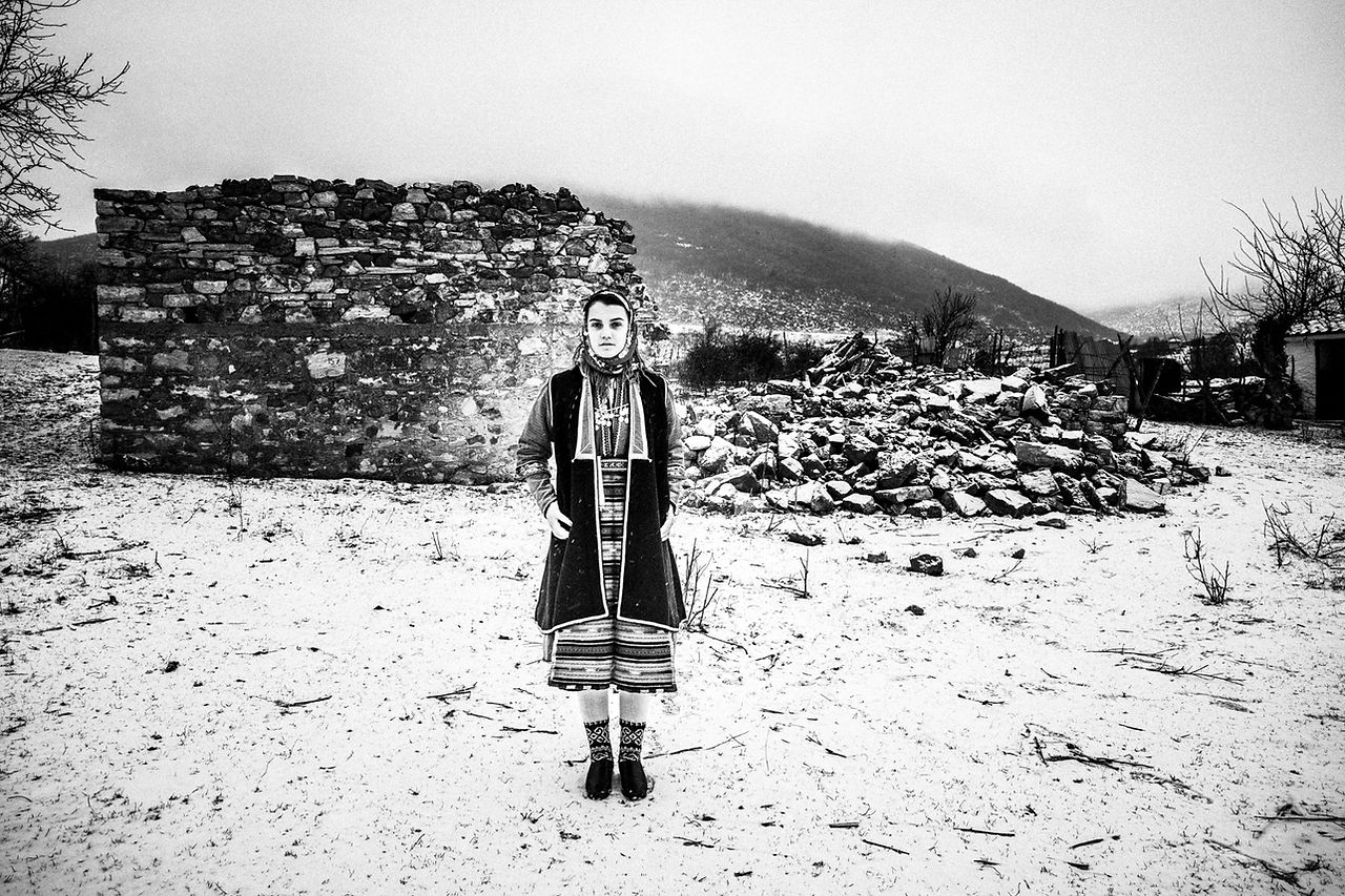 A woman in the local dress, posing in the snow. Volax, Macedonia, Greece. Black and white photograph by George Tatakis
