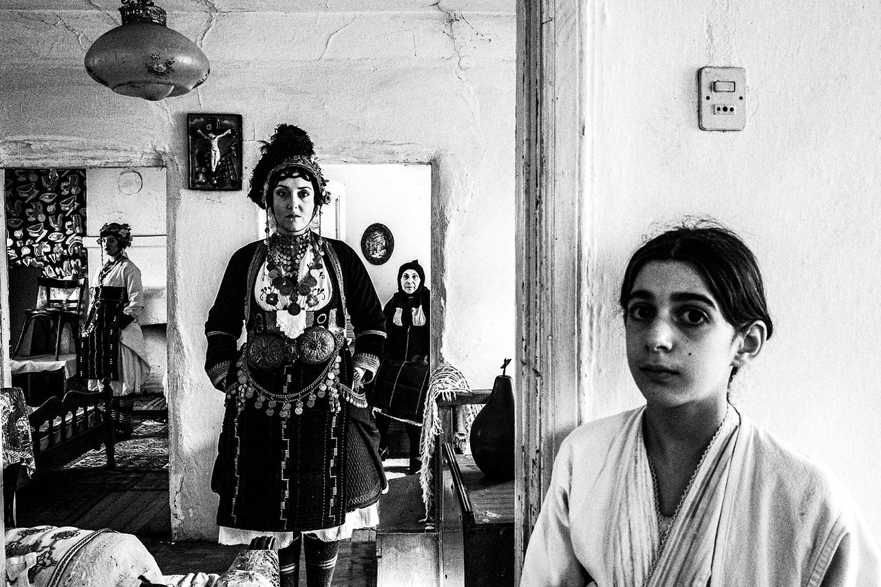 A group of women wearing the Roumlouki folklore dresses, inside a local traditional home. Meliki, Imathia, Macedonia, Greece. Black and white photograph by George Tatakis