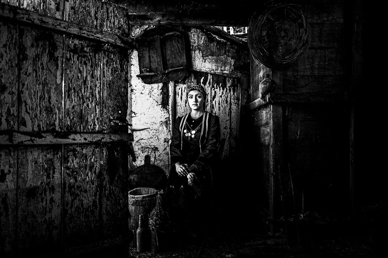 Sitting portrait of a woman in an old house, wearing the local attire. Lefki, Kastoria, Macedonia, Greece. Black and white photograph by George Tatakis