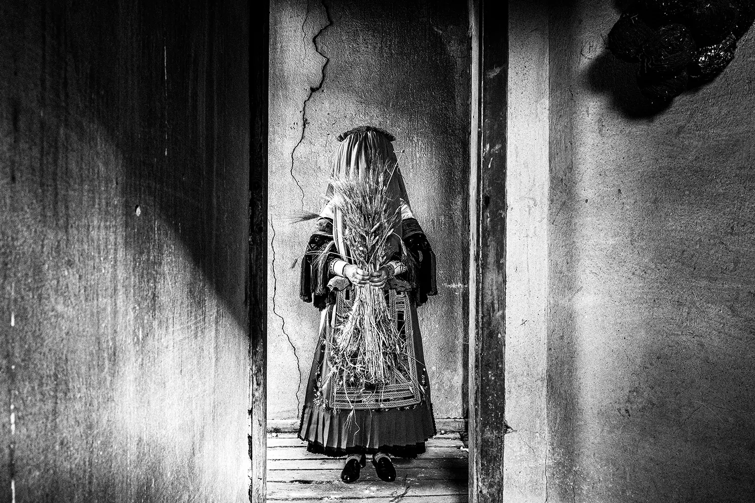 A Karagouna bride holding a bouquet of wheat in Glinos, Trikala, Thessaly, Greece. Black and white photography by George Tatakis