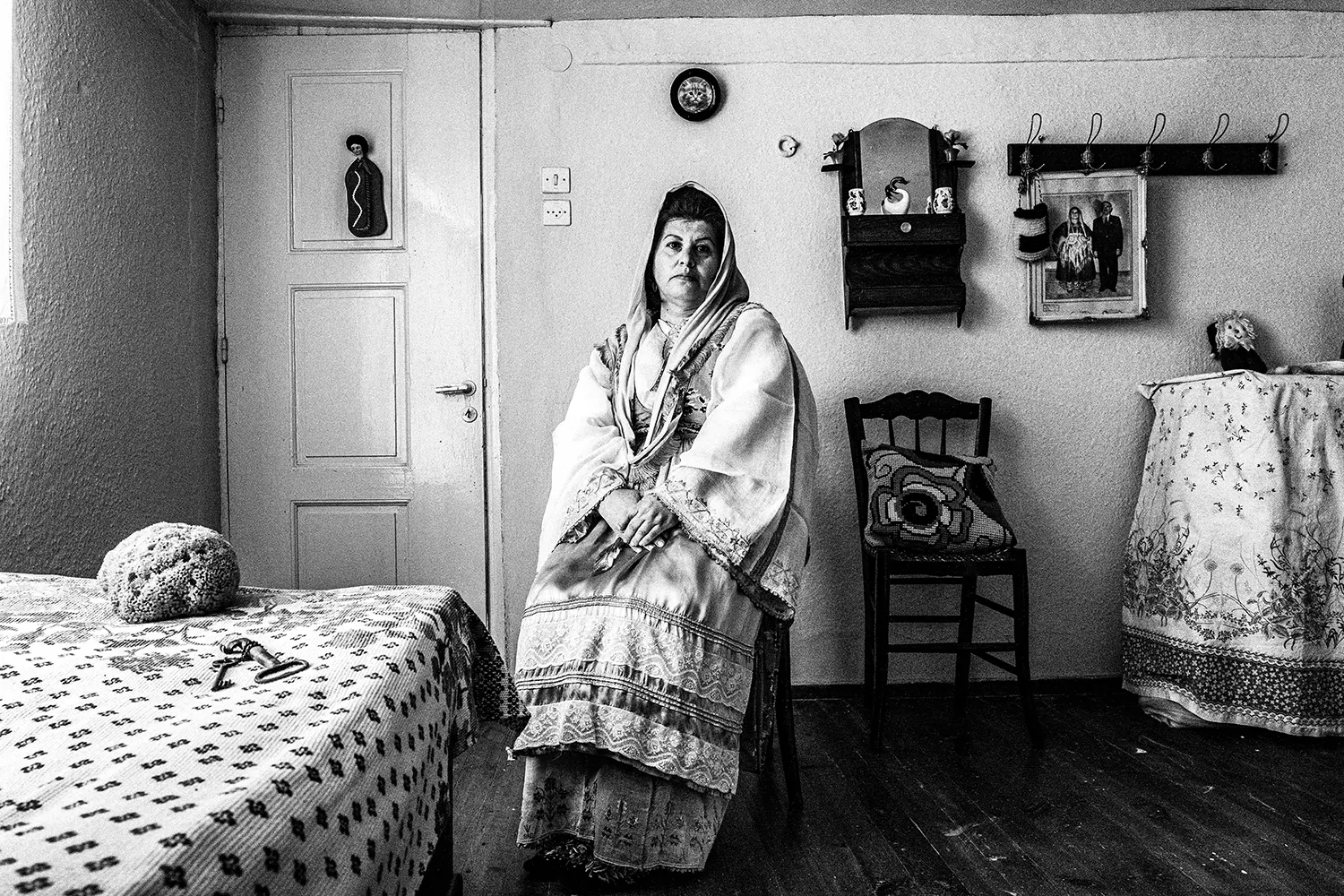 Portrait of a woman sitting inside a traditional home, wearing the folklore dress of Trikeri, Thessaly, Greece. Black and white photography by George Tatakis
