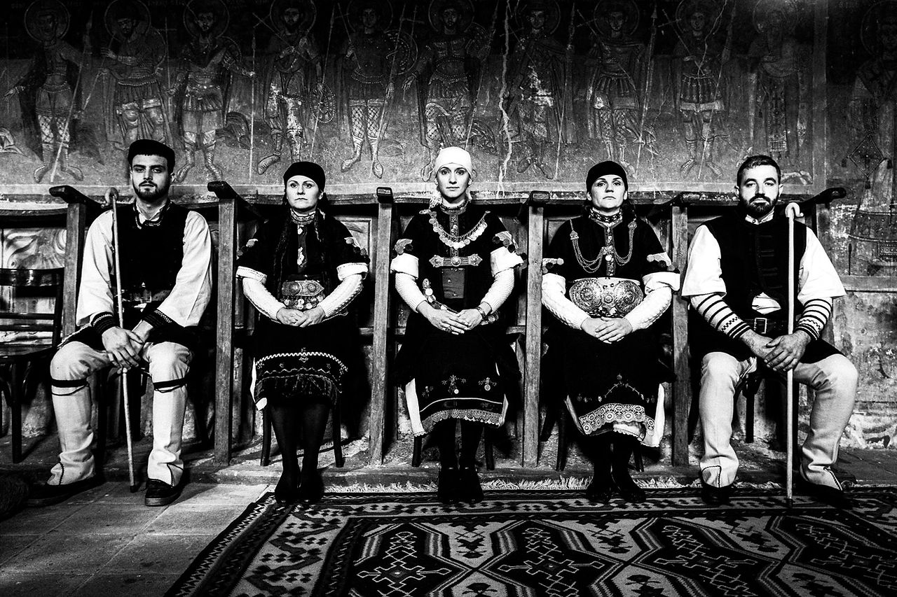 A row of five persons, sitting inside a local church. Prespes, Macedonia, Greece. Black and white photograph by George Tatakis