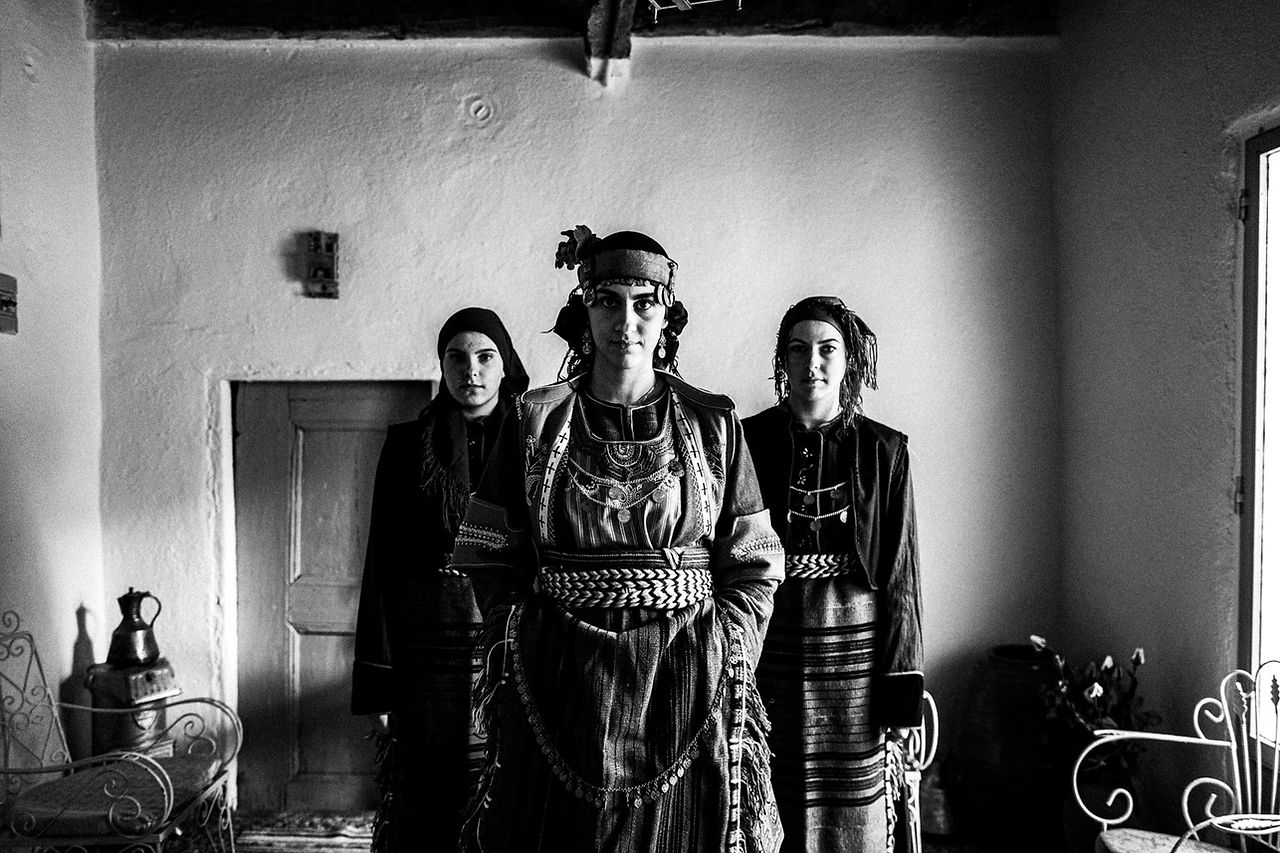 Three women inside a local home, wearing the traditional costumes. Drymos, Thessaloniki, Macedonia, Greece. Black and white photograph by George Tatakis