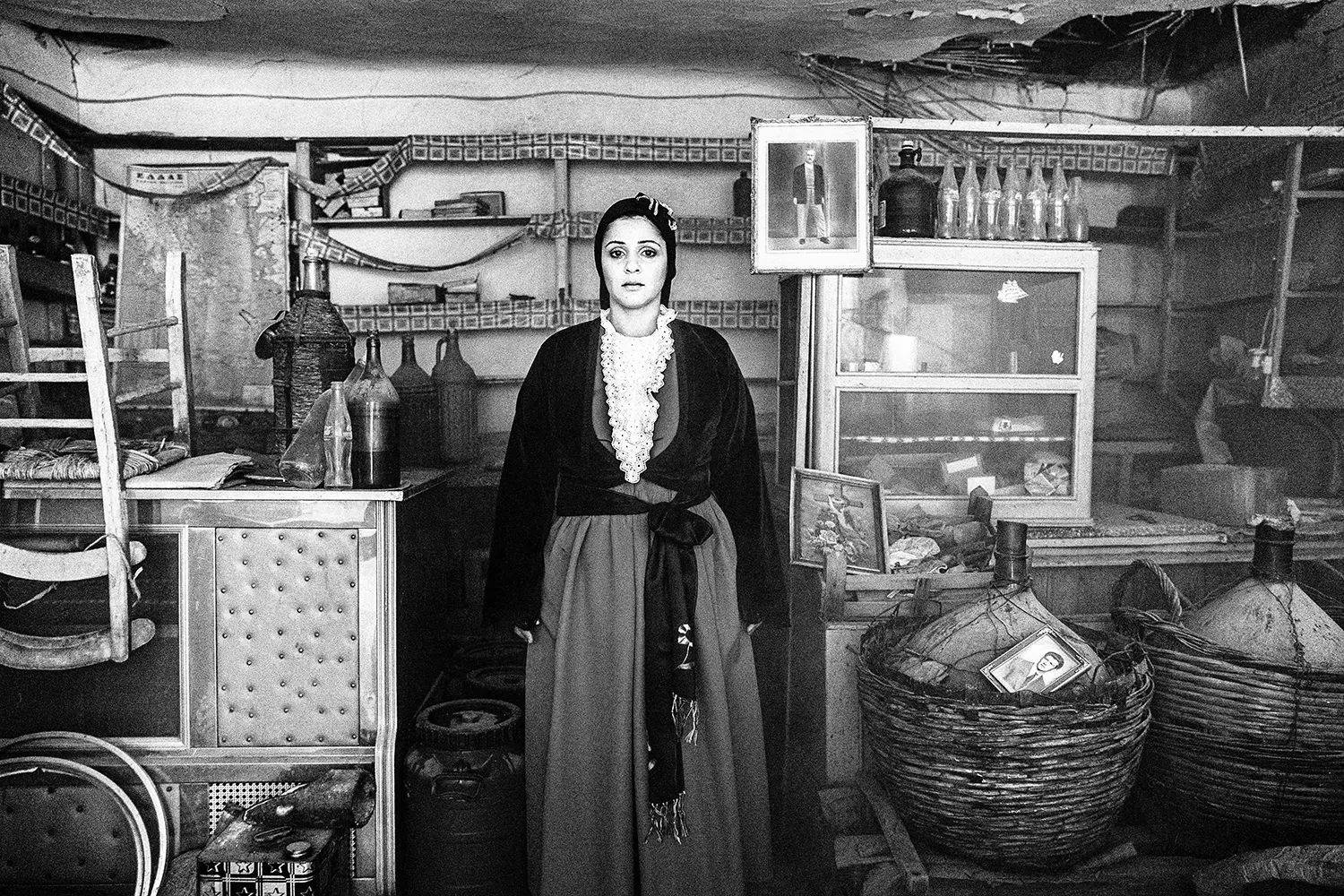 A woman in an abandoned shop in Portaria, wearing the local urban dress of Pelion, Thessaly, Greece. Black and white photography by George Tatakis