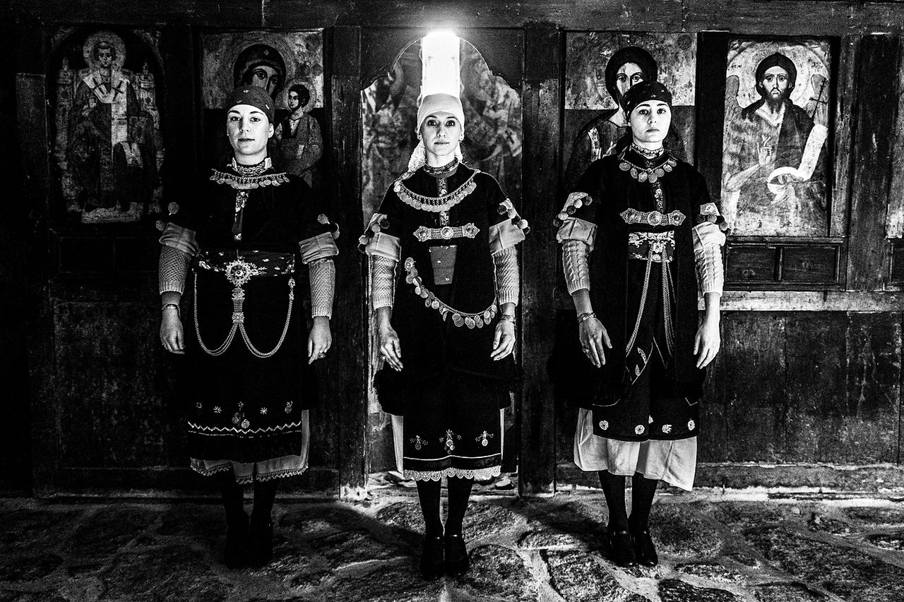 Three women one next to the other inside a local church, wearing the traditional costumes. Prespes Lakes, Macedonia, Greece. Black and white photograph by George Tatakis