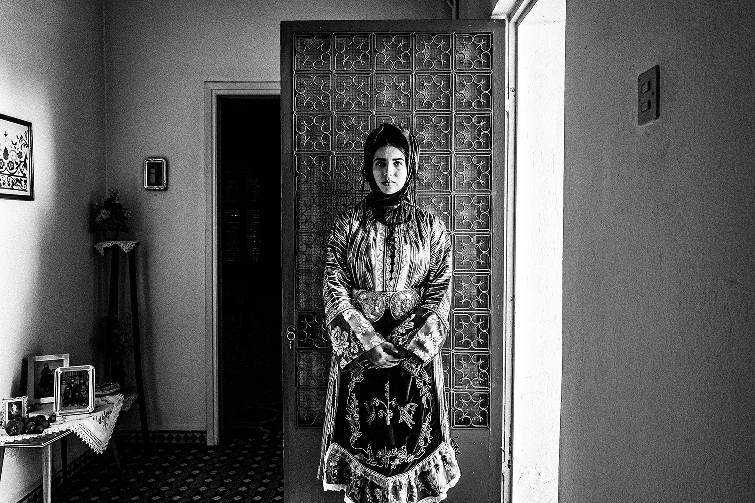A woman in front of a door, wearing the local costume of Stefanovikio, Thessaly, Greece. Black and white photography by George Tatakis.