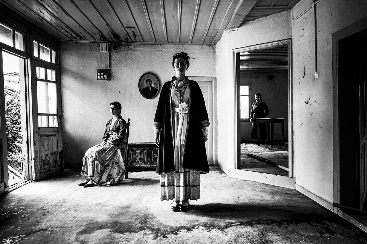 Three women inside an abandoned house, wearing the local urban folklore dresses of Veria, Imathia, Macedonia, Greece. Black and white photograph by George Tatakis