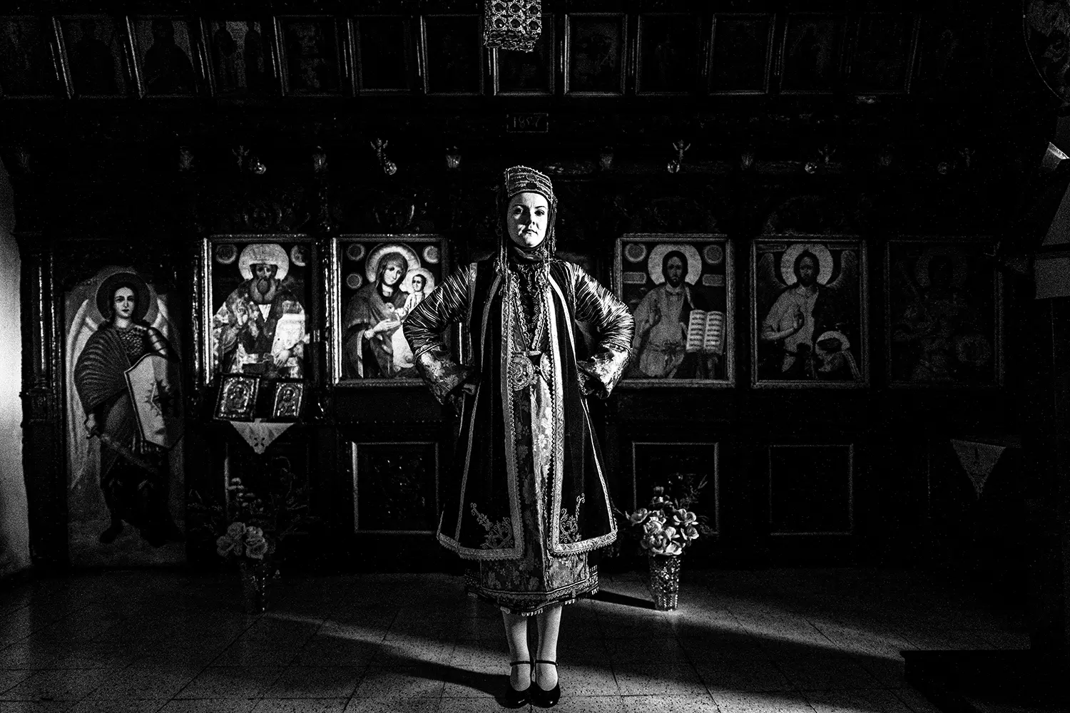 A woman inside a church, wearing the local traditional costume of Stefanovikio, Thessaly, Greece. Black and white photography by George Tatakis.