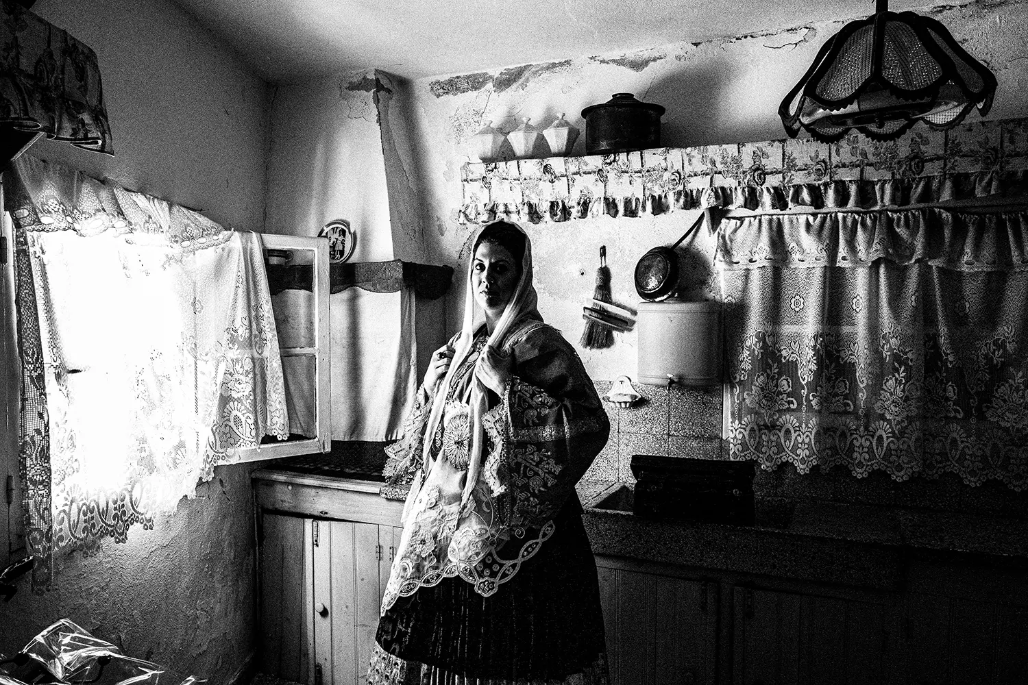 A woman dressed in the folklore bridal dress, inside a traditional kitchen in Trikeri, Thessaly, Greece. Black and white photography by George Tatakis