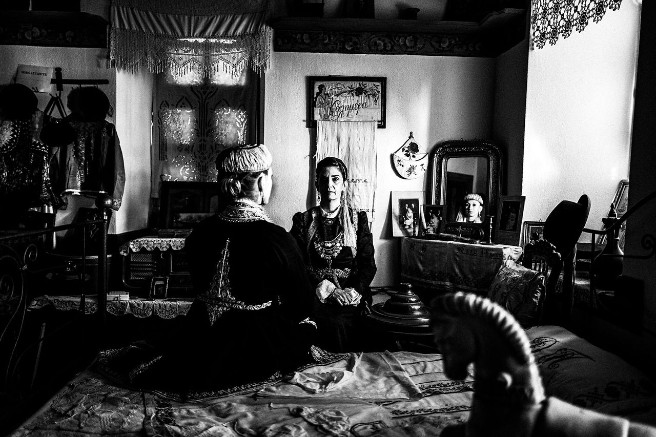 Two women inside the bedroom of a Mansion in Siatista, wearing the folklore dresses of Kozani, Macedonia, Greece. Black and white photograph by George Tatakis