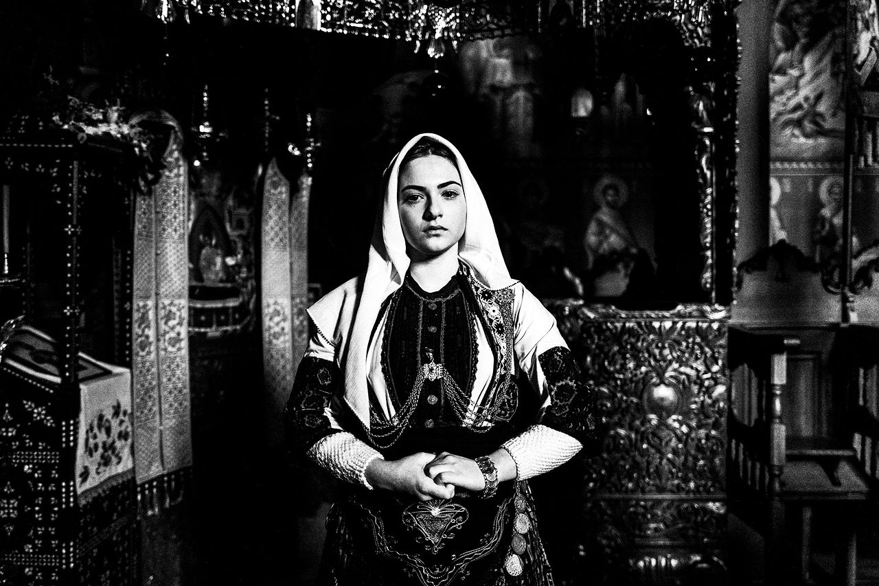 Portrait of a woman inside the local Monastery's church, wearing the traditional costume of the area. Kladorachi, Florina, Macedonia, Greece. Black and white photograph by George Tatakis
