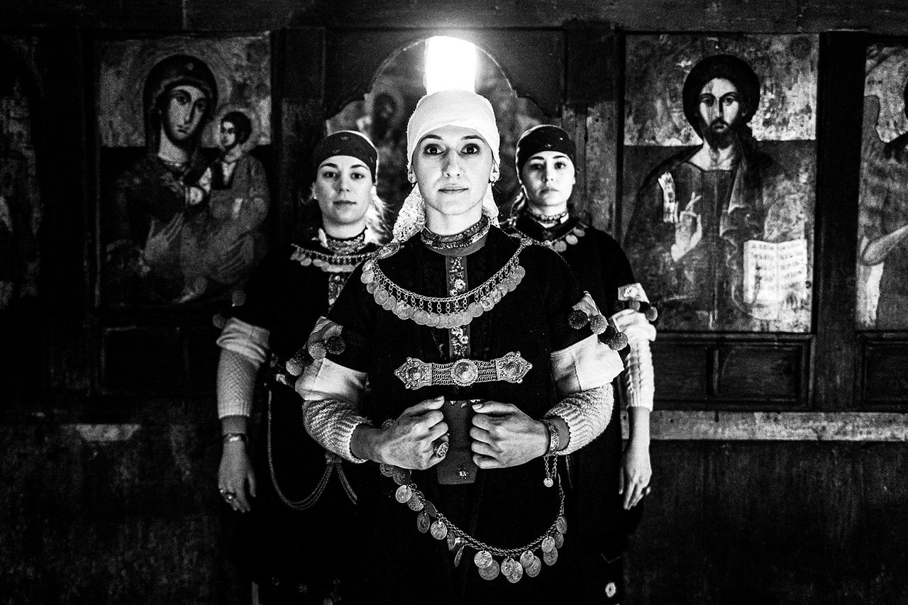 Three women in the local attire of Prespes, inside a local church. Macedonia, Greece. Black and white photograph by George Tatakis