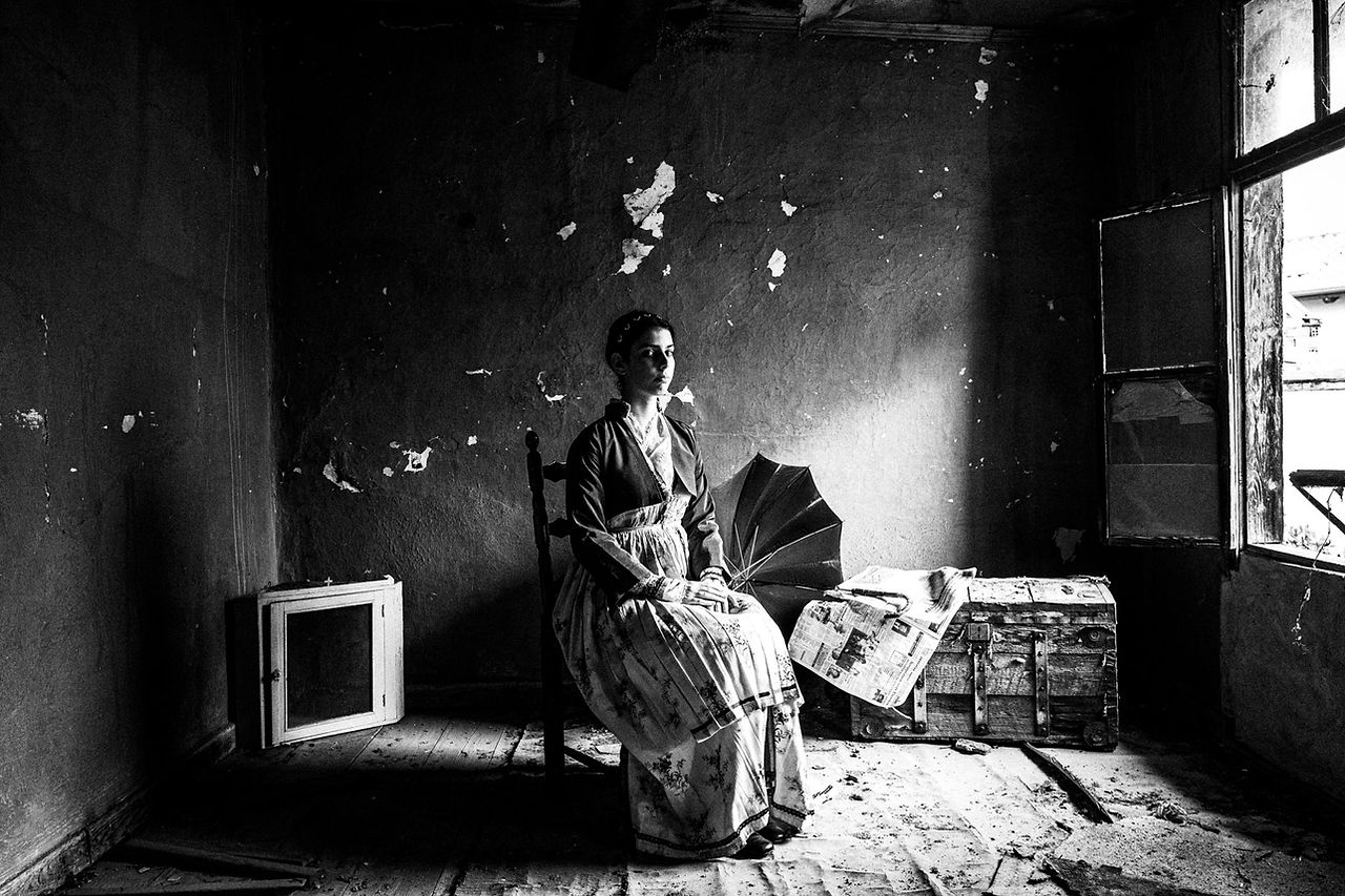 Sitting portrait of a woman inside the room of a local traditional home in Veria, Imathia, Macedonia, Greece. Black and white photograph by George Tatakis