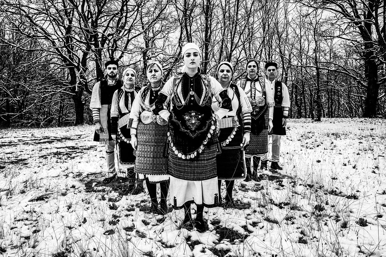 A group of locals in an arrow formation at a snowy forest, wearing the traditional costumes. Kladorachi, Florina, Macedonia, Greece. Black and white photograph by George Tatakis