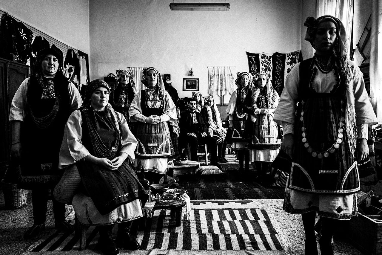 A group of ten persons inside the local folklore museum, wearing the local attire. Skopos, Florina, Macedonia, Greece. Black and white photograph by George Tatakis