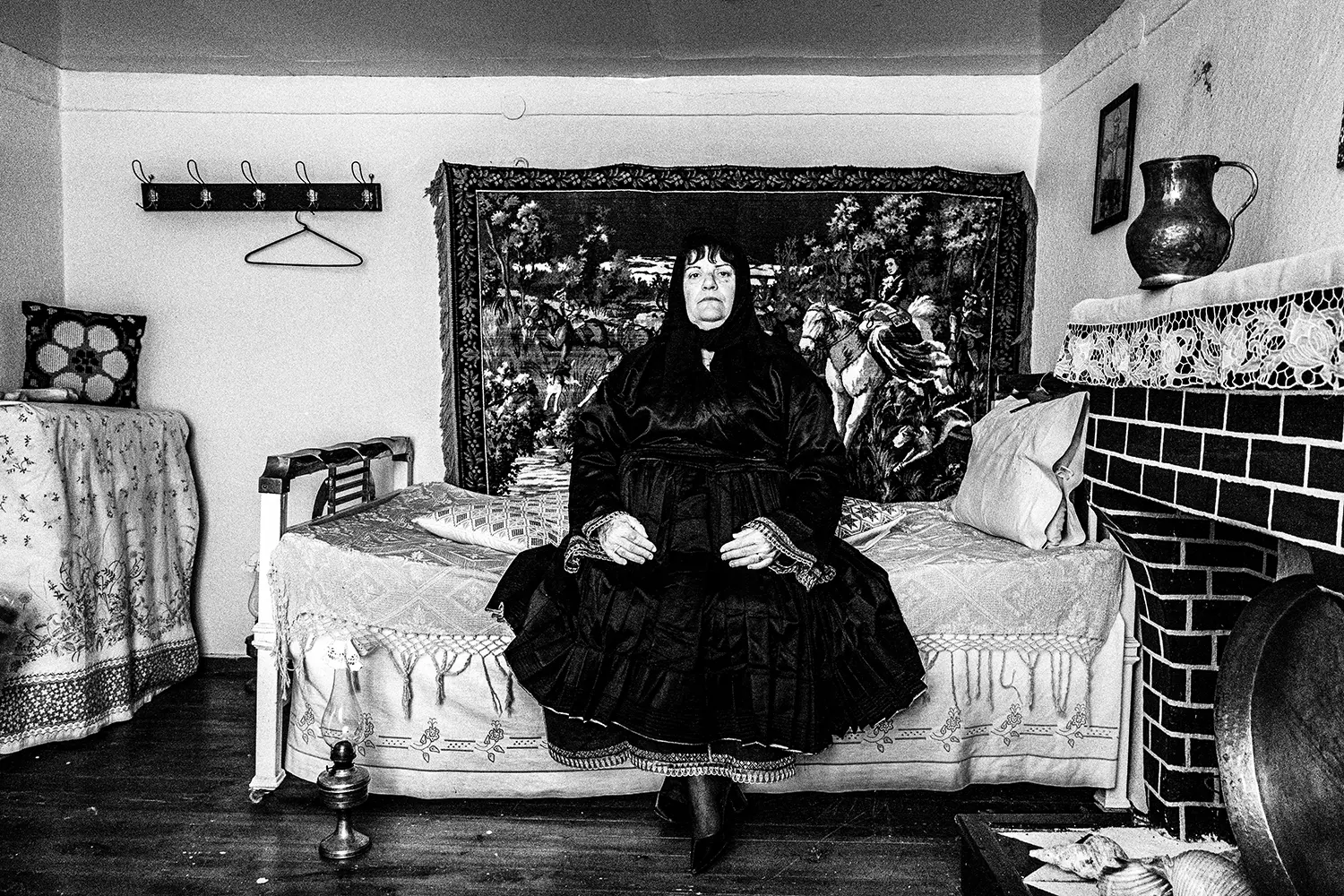 A woman in black traditional clothes sitting on a bed in Trikeri, Thessaly, Greece. Black and white photography by George Tatakis