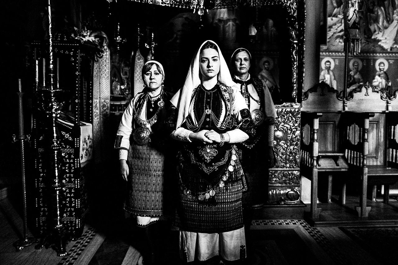 Three women inside the church of the local Monastery, wearing the traditional attire. Kladorachi, Florina, Macedonia, Greece. Black and white photograph by George Tatakis