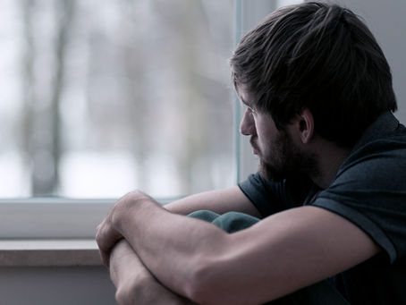Un hombre mirando por una ventana pensativo, porque no se siente y encuentra bien.